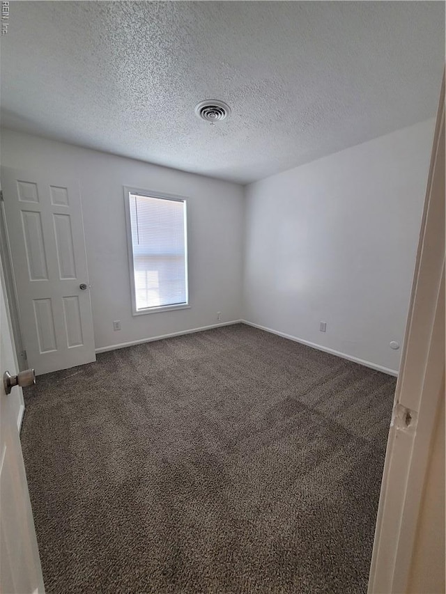 empty room with dark colored carpet, a textured ceiling, and visible vents