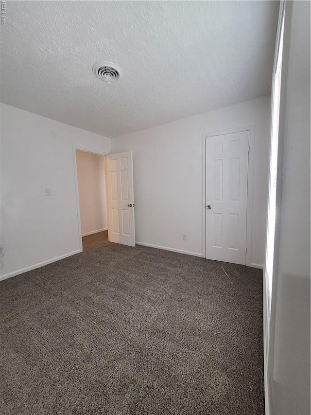 spare room featuring a textured ceiling, visible vents, baseboards, and dark colored carpet