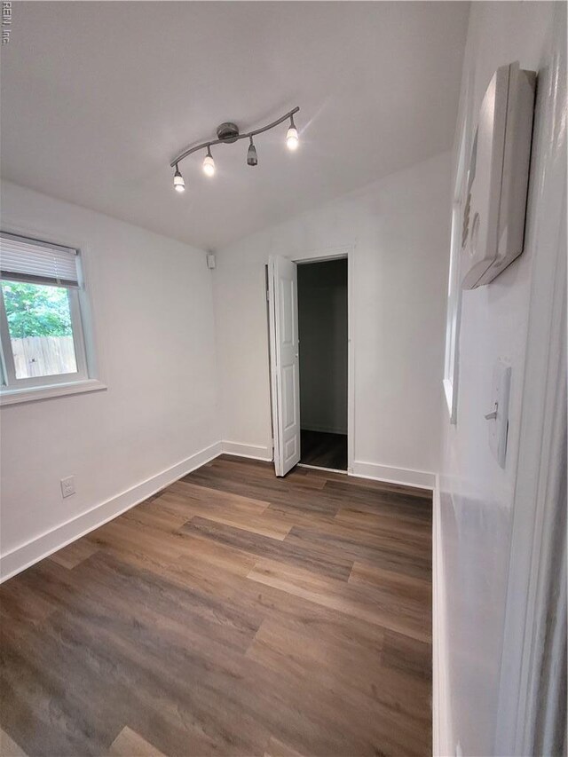 unfurnished bedroom with baseboards, rail lighting, and wood finished floors