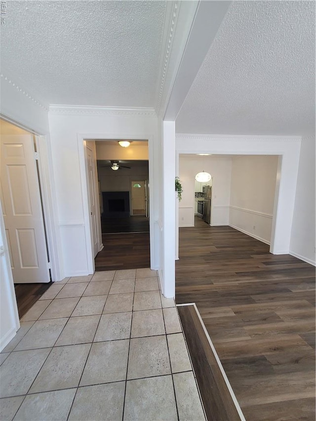 hallway with crown molding, a textured ceiling, baseboards, and light wood-type flooring