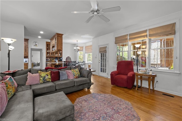 living area featuring recessed lighting, ceiling fan with notable chandelier, light wood-type flooring, and visible vents