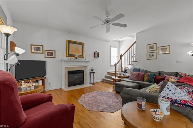 living area with stairs, ceiling fan, wood finished floors, and a glass covered fireplace