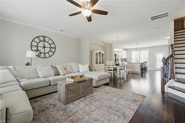 living room featuring visible vents, stairs, baseboards, dark wood-style floors, and ceiling fan with notable chandelier