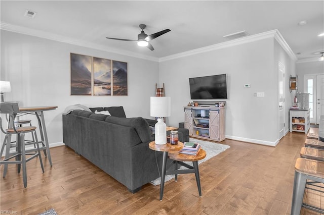 living area featuring crown molding, a ceiling fan, baseboards, and visible vents