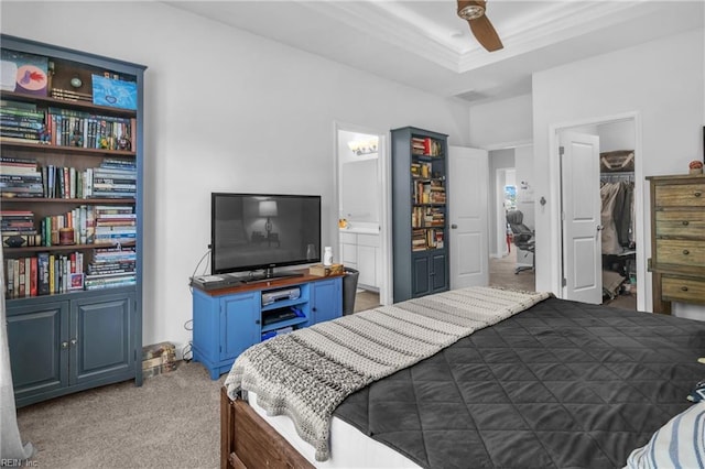carpeted bedroom featuring crown molding, ensuite bathroom, a walk in closet, a raised ceiling, and a ceiling fan