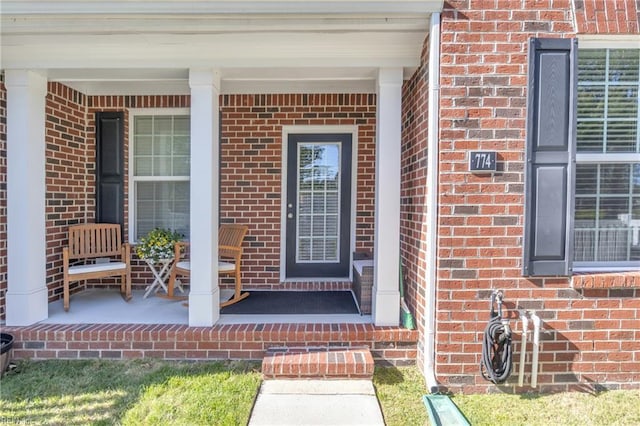 view of exterior entry featuring a porch and brick siding