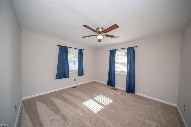carpeted spare room featuring baseboards, a ceiling fan, and visible vents