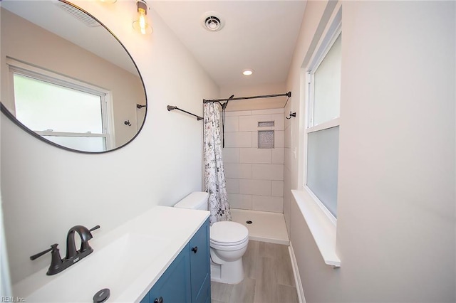 bathroom with visible vents, vanity, wood finished floors, toilet, and a tile shower