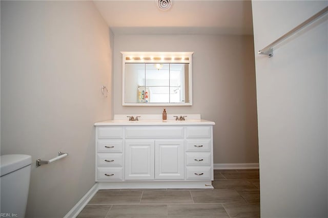 bathroom with double vanity, baseboards, toilet, and a sink