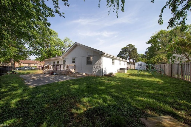 back of house with a deck, a fenced backyard, a patio area, a playground, and a lawn