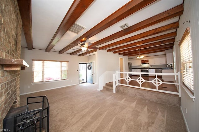 living room featuring carpet flooring, beam ceiling, a fireplace, a ceiling fan, and visible vents