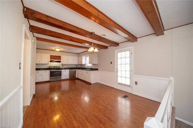 kitchen featuring dark countertops, beam ceiling, a wainscoted wall, stainless steel appliances, and visible vents