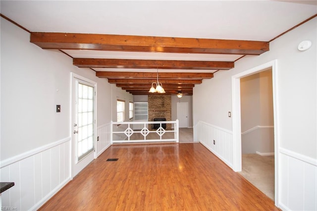 unfurnished room with a wainscoted wall, beam ceiling, wood finished floors, and a notable chandelier