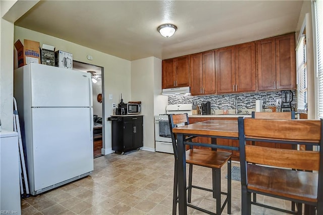 kitchen with backsplash, brown cabinets, a sink, under cabinet range hood, and white appliances