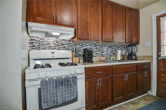 kitchen with a sink, light countertops, under cabinet range hood, white gas range oven, and backsplash