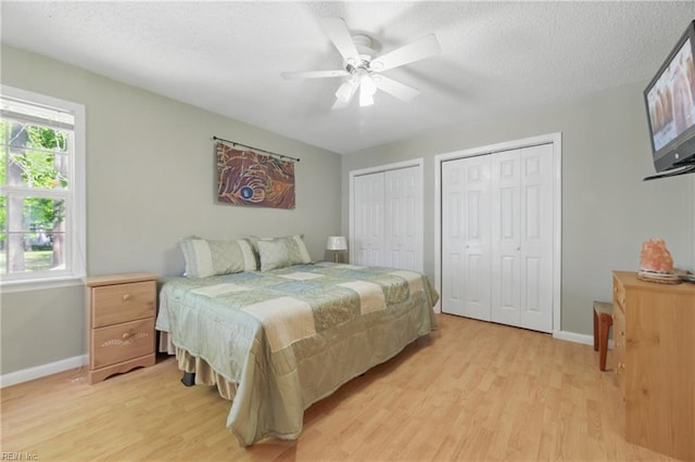 bedroom featuring two closets, a textured ceiling, baseboards, and light wood finished floors