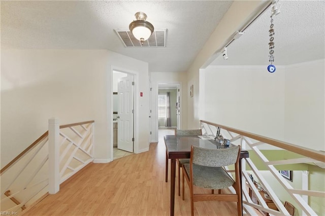 corridor featuring a textured ceiling, visible vents, an upstairs landing, and light wood-style floors