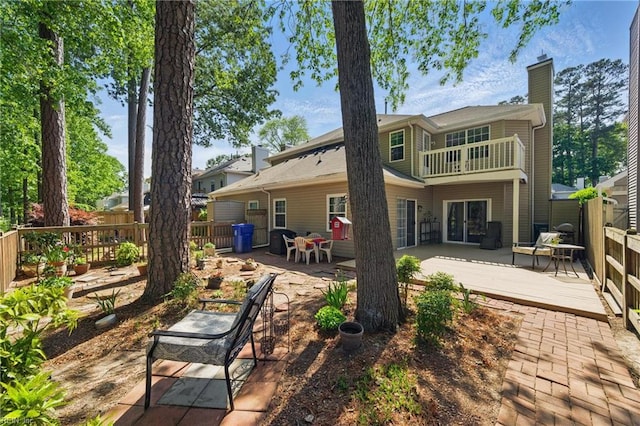 rear view of house with a wooden deck, fence, a balcony, a chimney, and a patio area
