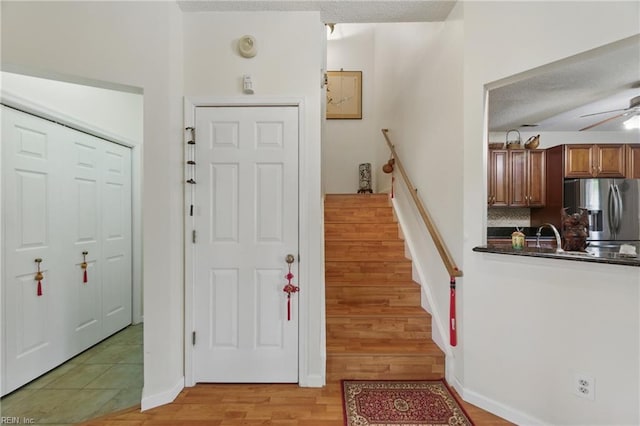entryway featuring stairway, baseboards, a ceiling fan, and light wood-style flooring