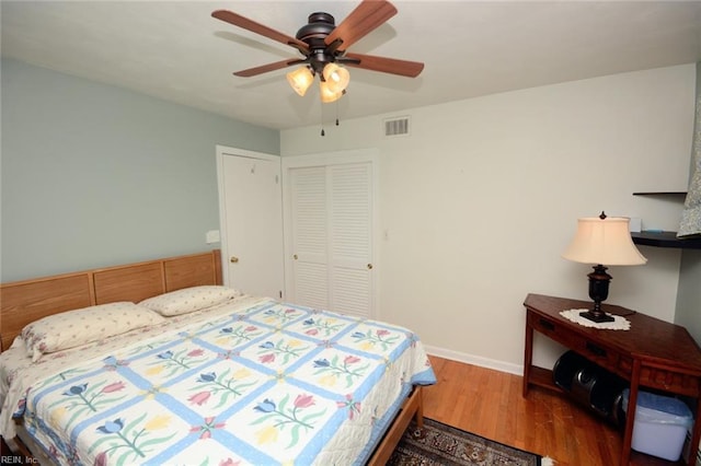 bedroom featuring ceiling fan, visible vents, wood finished floors, baseboards, and a closet
