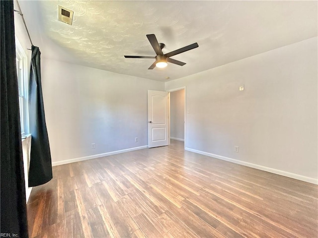 unfurnished room with a ceiling fan, baseboards, visible vents, and wood finished floors