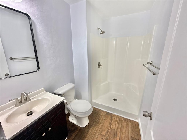 bathroom with vanity, toilet, wood finished floors, and a shower