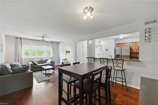 dining area featuring dark wood-type flooring, a textured ceiling, baseboards, and visible vents