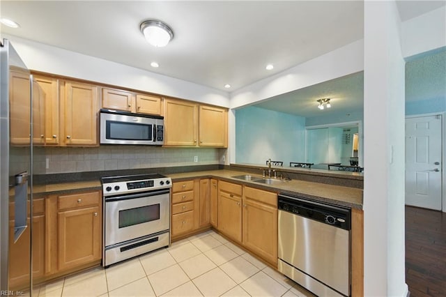 kitchen with stainless steel appliances, dark countertops, a sink, and tasteful backsplash