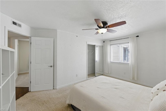 carpeted bedroom with visible vents, a closet, baseboards, ceiling fan, and a textured ceiling