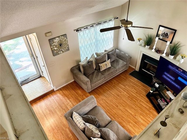 living room with ceiling fan, a textured ceiling, a fireplace with flush hearth, wood finished floors, and baseboards