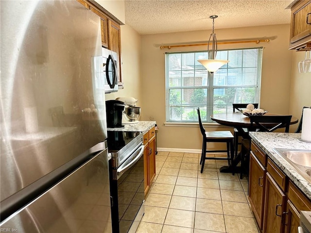 kitchen featuring a textured ceiling, brown cabinetry, stainless steel appliances, decorative light fixtures, and light tile patterned floors