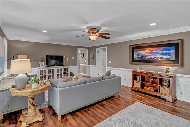 living area featuring wood finished floors, ornamental molding, a ceiling fan, and a wainscoted wall