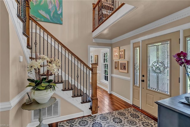 foyer entrance with wood-type flooring, stairs, baseboards, visible vents, and ornamental molding