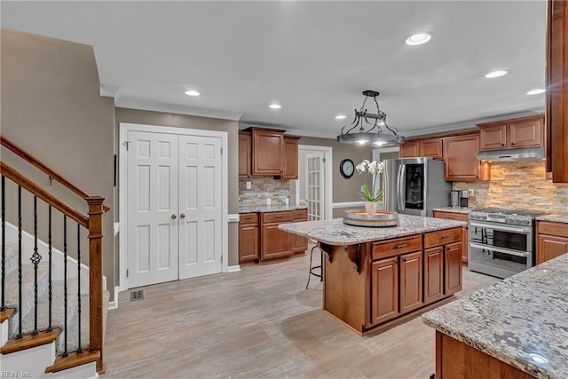 kitchen with brown cabinetry, stainless steel appliances, decorative backsplash, under cabinet range hood, and a kitchen island
