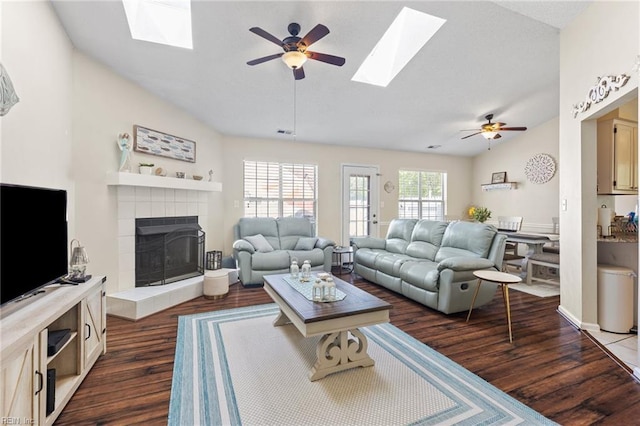 living area featuring ceiling fan, dark wood finished floors, a tile fireplace, and lofted ceiling with skylight