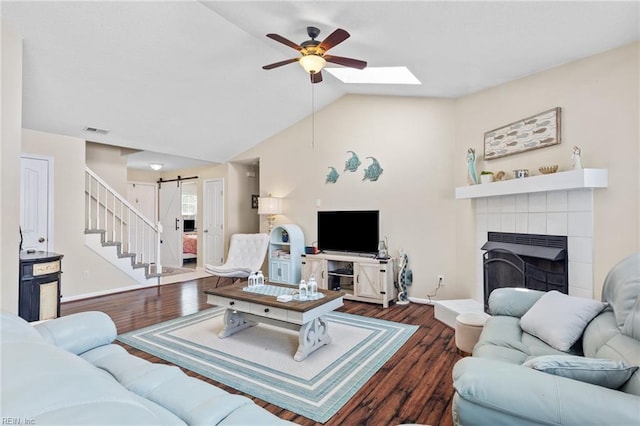 living room featuring ceiling fan, a barn door, vaulted ceiling with skylight, wood finished floors, and visible vents