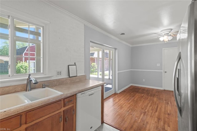 kitchen with brown cabinetry, light wood-type flooring, dishwasher, a sink, and freestanding refrigerator