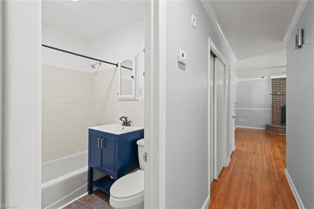 full bathroom with vanity, a brick fireplace, toilet, wood finished floors, and ornamental molding