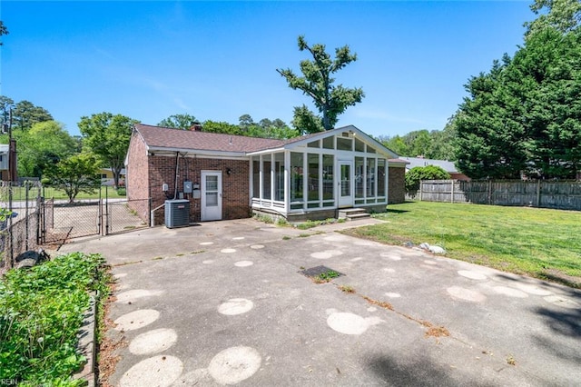 back of property with a sunroom, a gate, brick siding, central air condition unit, and a yard
