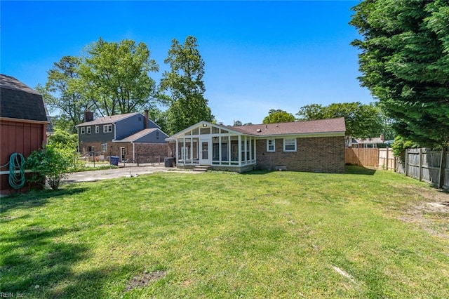 rear view of house featuring fence, brick siding, a sunroom, cooling unit, and a yard