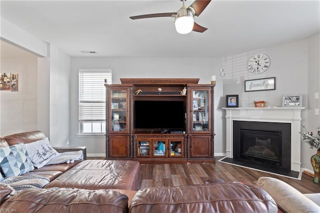living area with visible vents, a ceiling fan, a glass covered fireplace, and dark wood-style floors