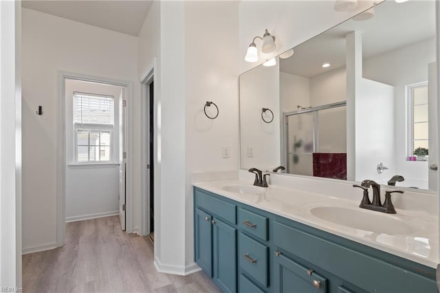 full bathroom featuring double vanity, a stall shower, a sink, and wood finished floors