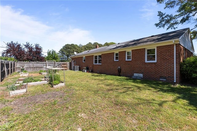 exterior space featuring a lawn, central AC unit, a vegetable garden, brick siding, and fence
