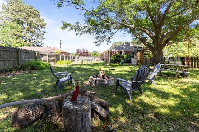 view of yard featuring a playground, a fenced backyard, and a fire pit