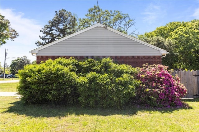 view of property exterior with a yard, brick siding, and fence