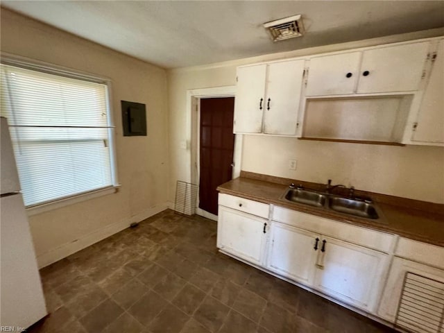kitchen with a sink, freestanding refrigerator, white cabinetry, visible vents, and electric panel