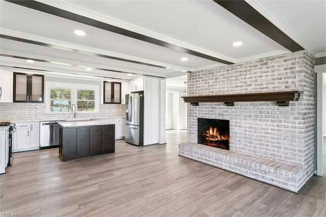 unfurnished living room with ornamental molding, beamed ceiling, a brick fireplace, and light wood-style flooring