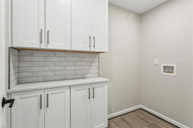 washroom with baseboards, hookup for a washing machine, cabinet space, and wood finished floors