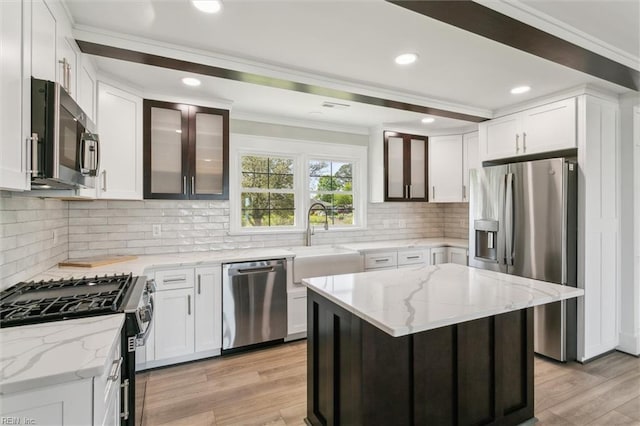 kitchen with crown molding, light stone counters, a sink, light wood finished floors, and appliances with stainless steel finishes