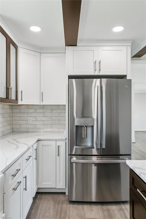 kitchen featuring light stone countertops, stainless steel refrigerator with ice dispenser, light wood-type flooring, white cabinetry, and tasteful backsplash